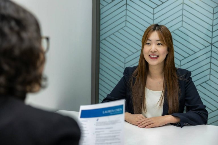 Confident, Beautiful Asian Woman in suit is smiling during a job interview in an office environment, explaining a career gap (without feeling awkward)