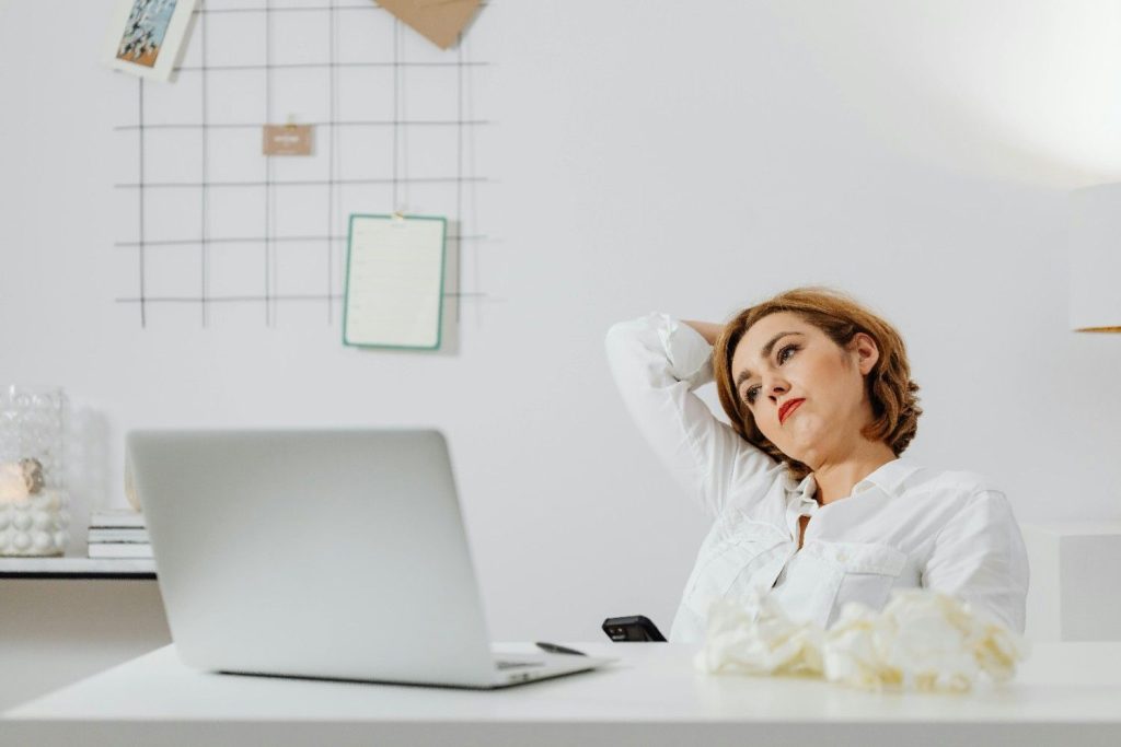 professional woman looking tired and contemplative at her desk, representing the psychological impact and emotional drain of company restructuring and job uncertainty.